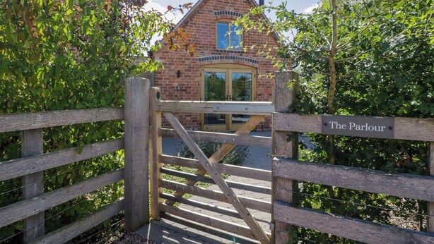 A wooden gate leading to a brick building with a sign reading "The Parlour". - The Parlour (Droitwich)