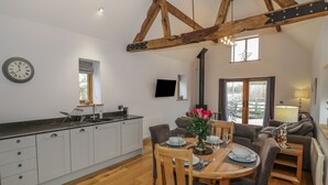A modern kitchen with white cabinets, a wooden dining table set for four, and a large window overlooking a garden. - The Parlour (Droitwich)