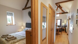 A bedroom with a bed, bedside table, and a window. There is a hallway leading to a dining area with a table and chairs. - The Parlour (Droitwich)