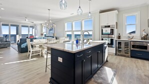 A modern kitchen with a large island, stainless steel appliances, and large windows offering ocean views. - Enjoy AMAZING VIEWS at almost new spacious oceanfront unit, huge deck, elevator (Carolina Beach)