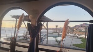 A room with a large arched window overlooking a pool area and a view of a mountain.