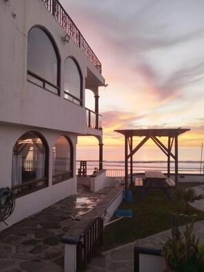 Un edificio de dos pisos con un balcón que da a una playa al atardecer.