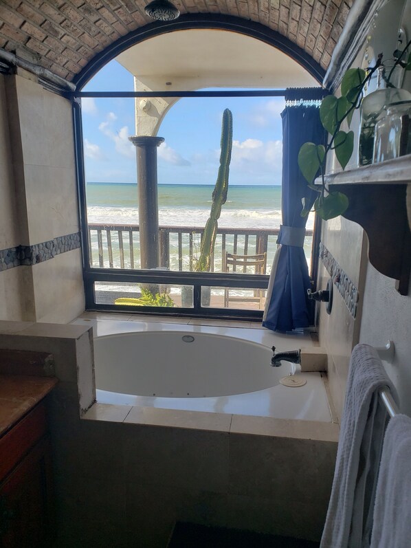 A bathroom with a large bathtub, a shower, and a view of the ocean.