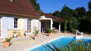 Area piscina con patio in pietra, piante in vaso e zona salotto coperta.