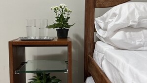 A wooden bedside table with a glass shelf, a potted plant, and a glass of water. - Melhores Flats (Cabedelo)