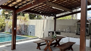 An outdoor patio with a pergola, a pool, and a kitchen area. - Melhores Flats (Cabedelo)