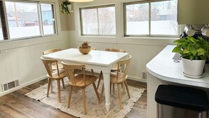 A dining area with a white table, wooden chairs, a hanging light fixture, and a potted plant. - Sunny Downtown Gunnison Retreat (Gunnison)