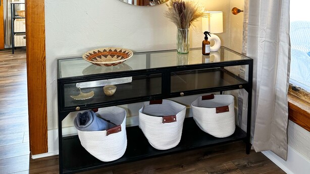 A room with a glass console table, a round mirror, a vase with dried plants, and a lamp. - Sunny Downtown Gunnison Retreat (Gunnison)