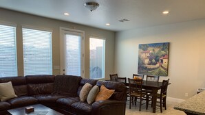 A living room with a dark brown leather sectional sofa, a wooden coffee table, and a dining area with a wooden table and chairs. - Spacious, Clean Coral Ridge Townhome (Washington)