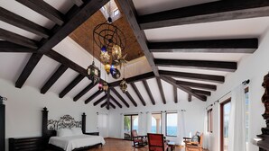 A spacious bedroom with a large bed, a wooden ceiling, and a view of the outdoors.