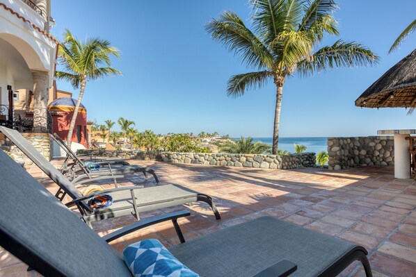 A patio with lounge chairs and a view of the ocean.