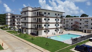 A multi-story residential building with a swimming pool, balconies, and a fire hydrant on the street.