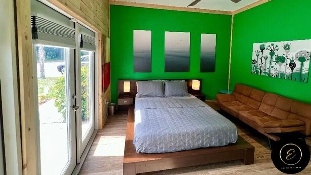 Un dormitorio con una cama, un sofá marrón, un ventilador de techo y una pared verde con tres espejos rectangulares.