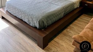 Un dormitorio moderno con techo de madera, una pared de acento verde, una cama grande con colcha gris, dos lámparas de noche y vistas al exterior a través de un ventanal.