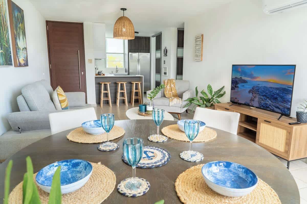 Un salon moderne avec un coin repas, comprenant un grand téléviseur, des sièges confortables et une cuisine en arrière-plan.