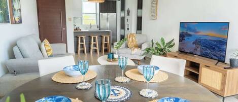 Una sala de estar moderna con comedor, que cuenta con un televisor grande, asientos cómodos y una cocina al fondo.