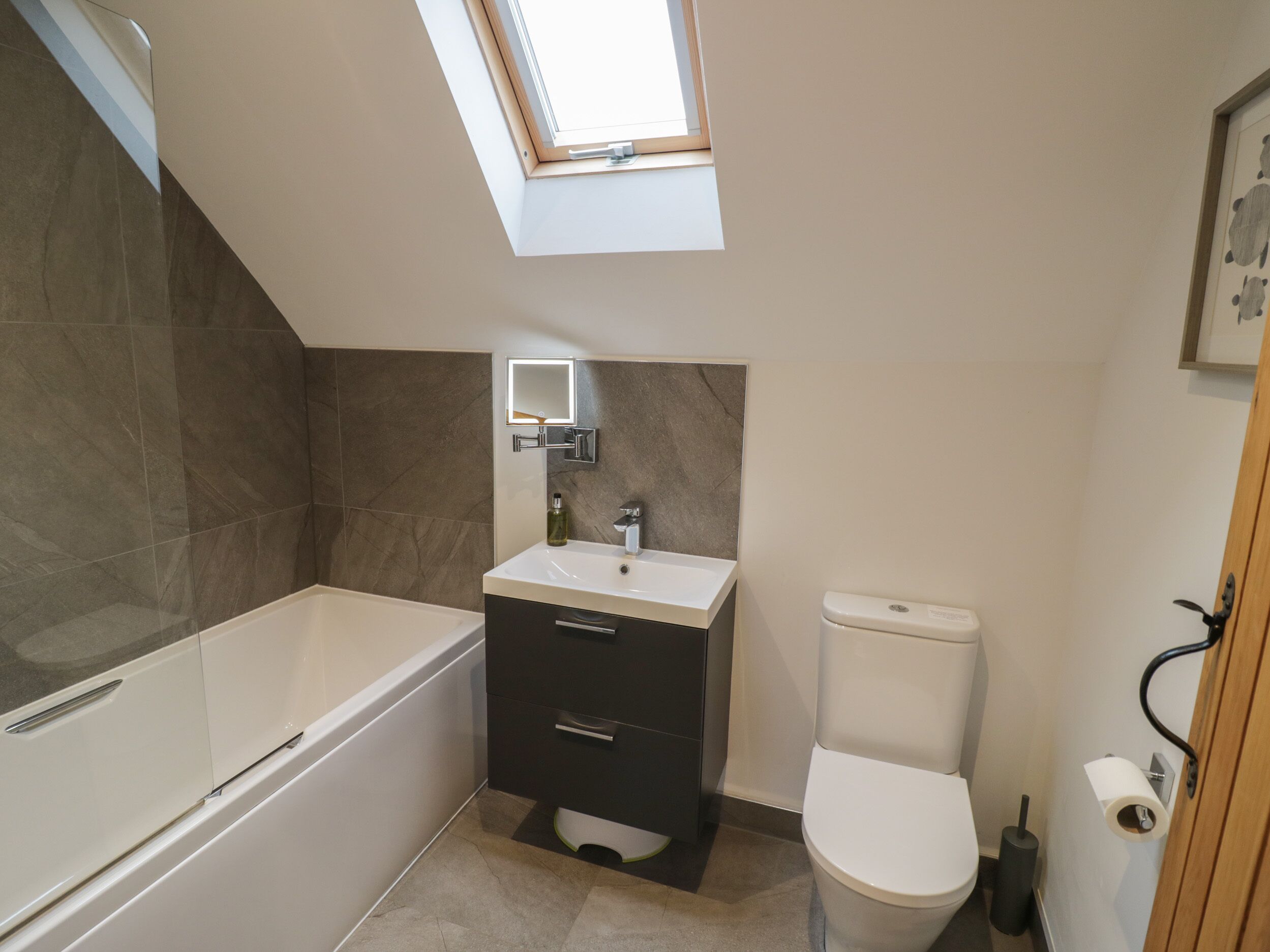 Une petite salle de bain dotée d’un puits de lumière, d’une baignoire, d’un lavabo et de toilettes.