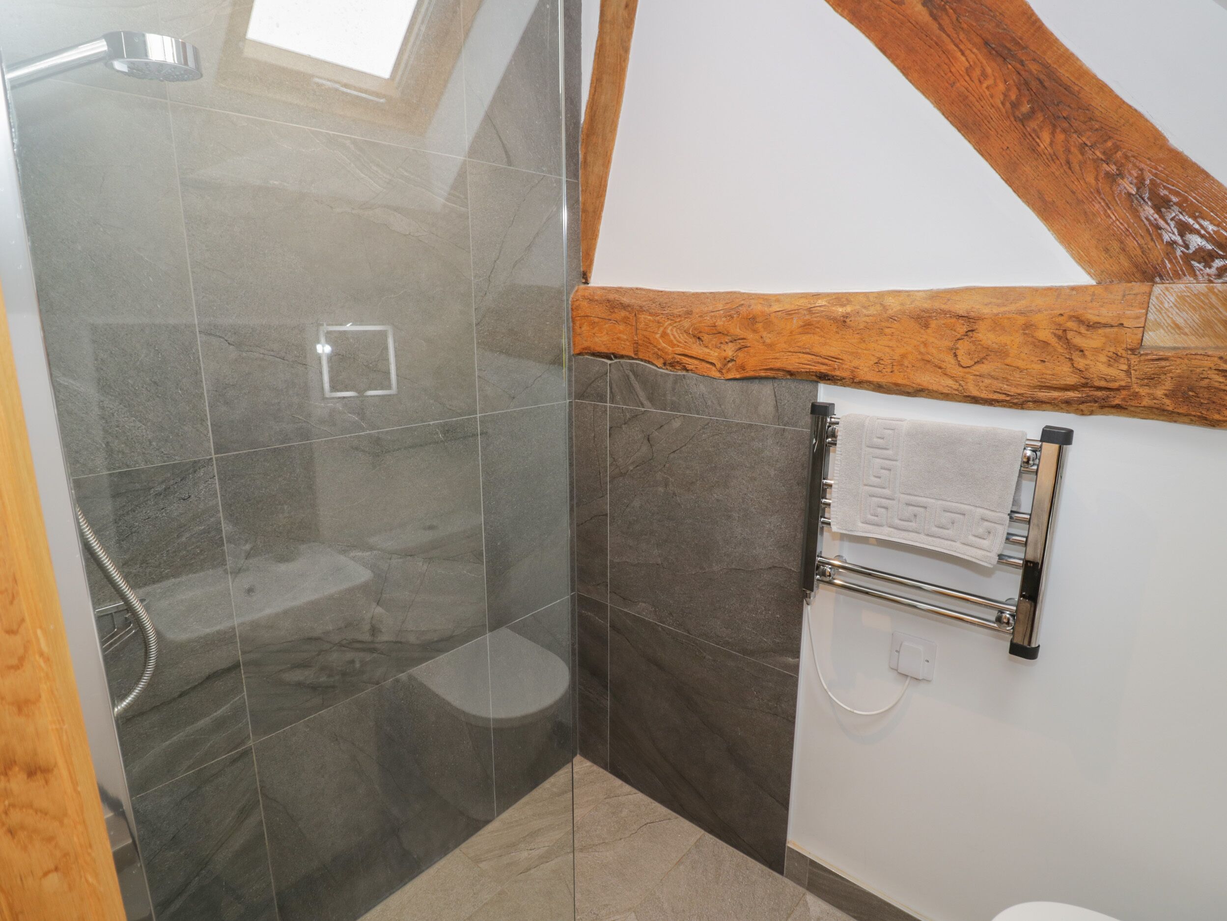 Un baño moderno con cabina de ducha de vidrio, techo de madera y toallero con una toalla estampada.