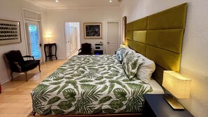 Et soveværelse med seng, ventilator, skrivebord, stol og dør.