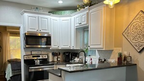 Een moderne keuken met witte kastjes, roestvrijstalen apparatuur, een centraal eiland met krukken en decoratieve wandkunst.