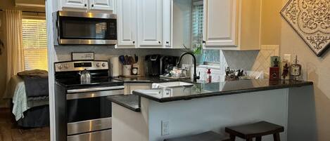 A modern kitchen with white cabinets, stainless steel appliances, a central island with stools, and decorative wall art.