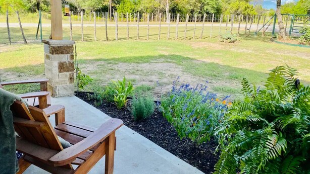 Een terras met een stenen pilaar, houten stoelen en een tuin vol planten en bloemen.