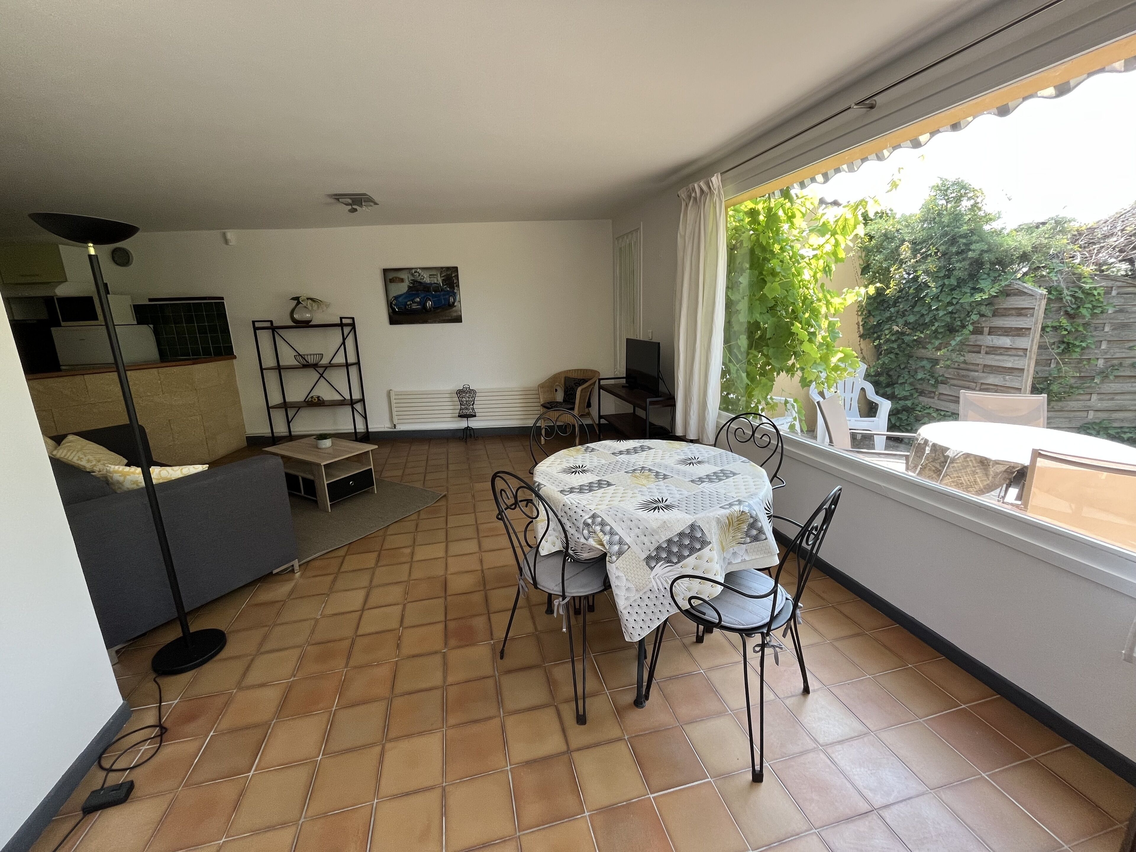 Una stanza con un tavolo da pranzo, sedie, un divano, una televisione e una finestra vista verde.