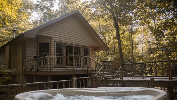 A cabin with a hot tub and a deck, surrounded by trees.