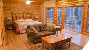 A log cabin room with a bed, a wooden table, a couch, and large windows.