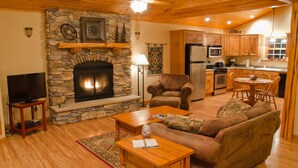 A cozy living room with a stone fireplace, wooden ceiling, and a television on a stand.