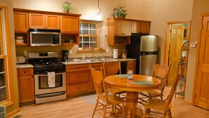 Une cuisine avec des meubles de rangement en bois, une cuisinière, un four à micro-ondes, un réfrigérateur et une table à manger avec des chaises.