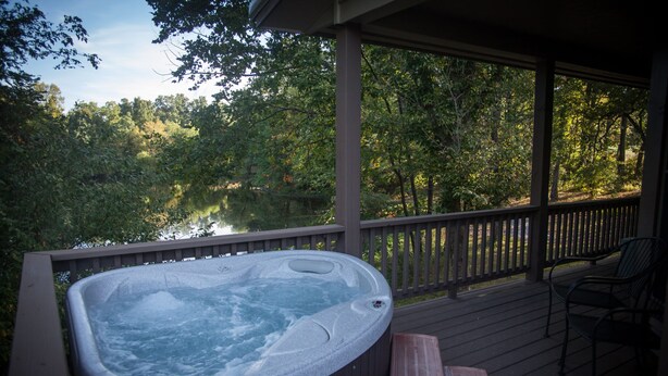 Un bain à remous sur une terrasse en bois, avec vue sur un lac et des arbres.