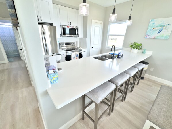 A modern kitchen with white cabinetry, stainless steel appliances, a large island with bar stools, and pendant lighting.