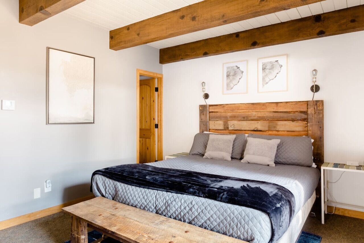 A bedroom with a wooden headboard, a bed with a quilted cover, a bench, and framed artwork on the wall.