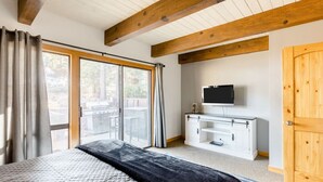 Une chambre dotée d’un grand lit, d’une télévision, d’une armoire en bois et d’une porte-fenêtre coulissante donnant sur un espace extérieur.