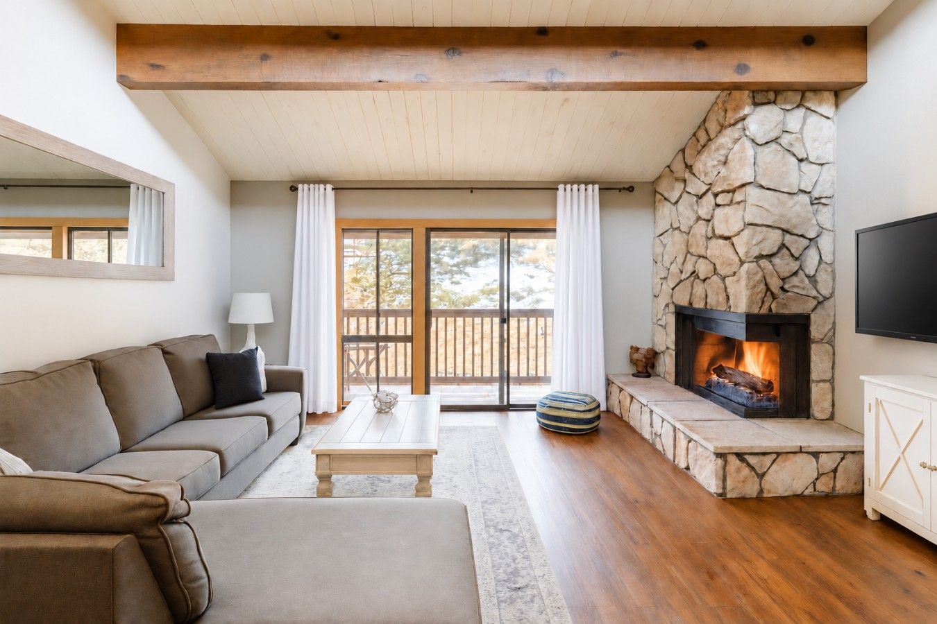 Cozy living room featuring a large, comfortable sofa, high ceilings, and a beautiful stone fireplace—perfect for relaxing after a day on the mountain. Step out onto the private balcony and enjoy incredible views where you can actually watch skiers coming