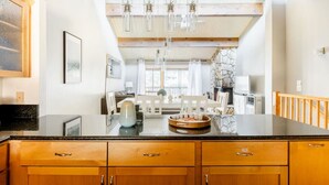 Une cuisine avec des meubles de rangement en bois, un plan de travail en marbre, des luminaires suspendus et un mur en pierre.