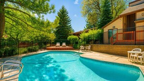 Une piscine avec des chaises longues et un espace de détente, entourée d’arbres et d’une terrasse délimitée par une clôture.