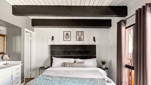A bedroom with a large bed, a nightstand, a dresser, and a window with curtains.
