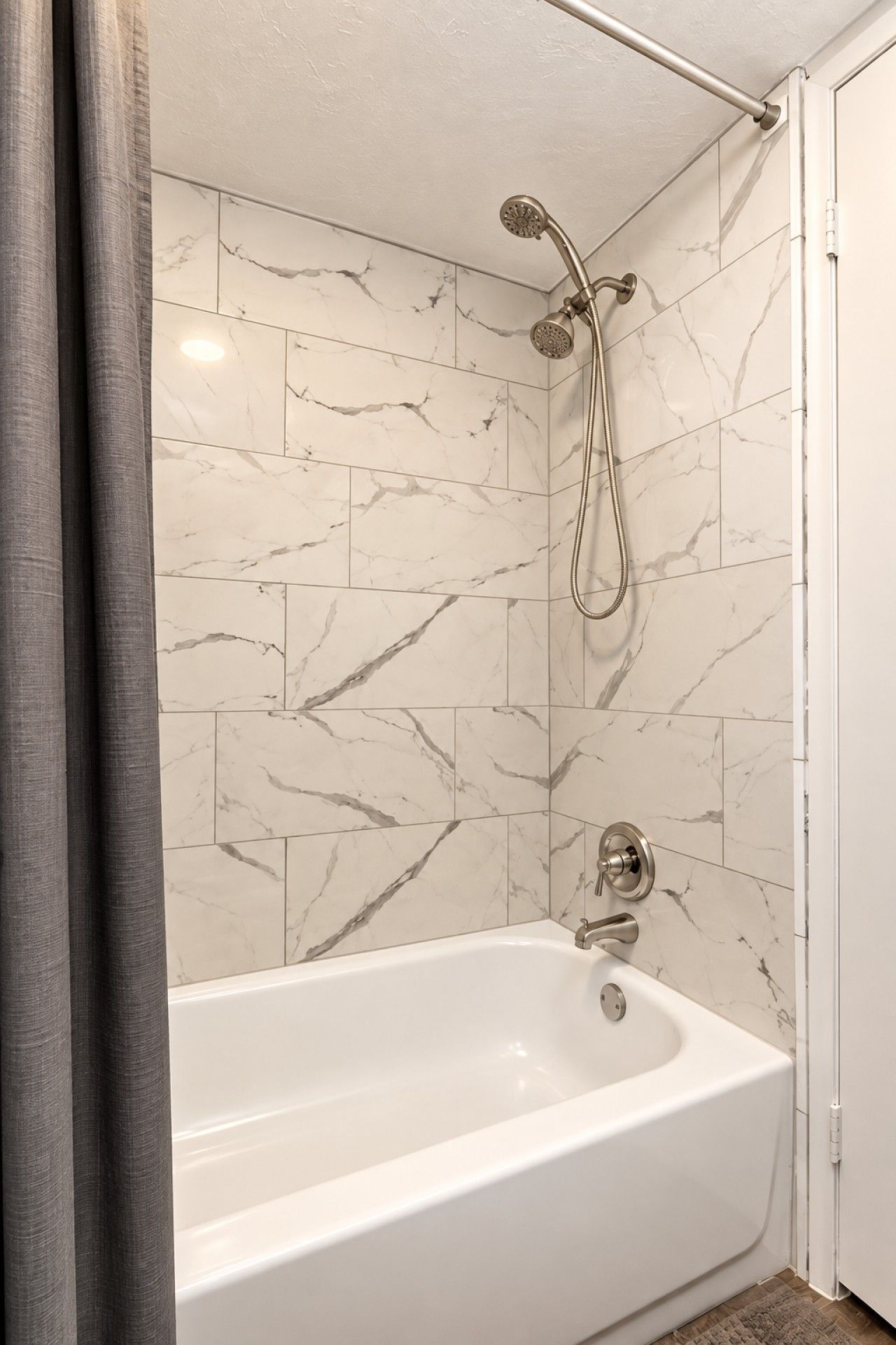 A bathroom with a white bathtub, a shower with a handheld showerhead, and marble-patterned tiles.
