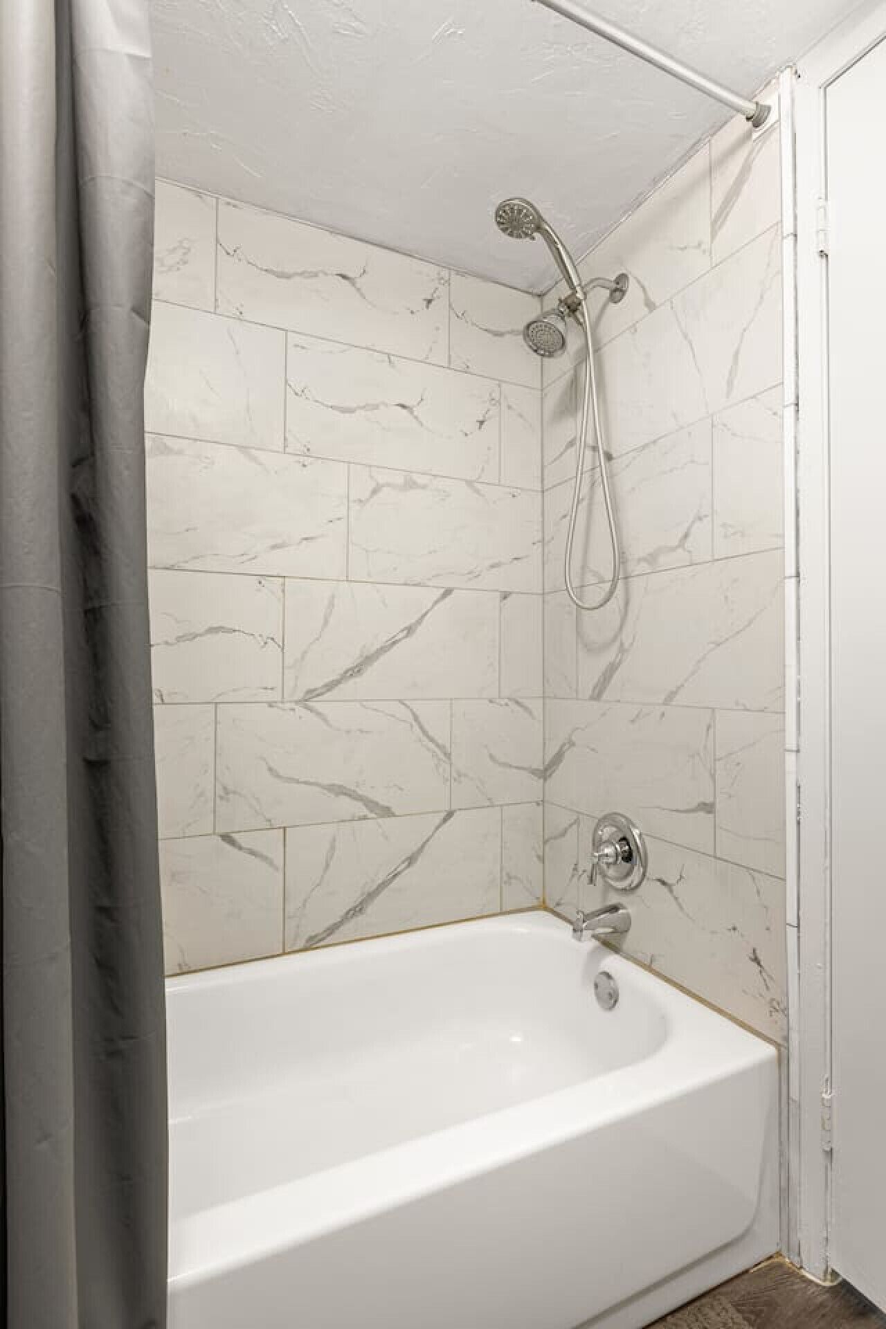 A bathroom with a white bathtub, a showerhead, and marble-patterned walls.