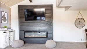 A modern living room with a fireplace, a mounted TV, and a round wall clock. - Feet Away From Slopes Cozy Snow Summit Cabin (Big Bear Lake)