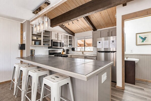Una cocina moderna con una isla grande, taburetes de bar, electrodomésticos de acero inoxidable y techo de madera.