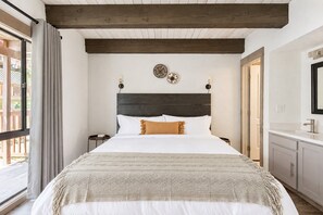 Un dormitorio con una cama grande, techo de madera, una mesita de noche, un reloj de pared y una ventana con cortinas.