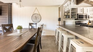 A modern kitchen with white cabinets, stainless steel appliances, and a wooden dining table with bar stools. - Feet Away From Slopes Cozy Snow Summit Cabin (Big Bear Lake)