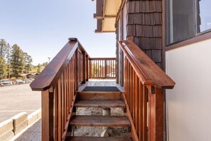 Eine Holztreppe führt zu einer Veranda mit Blick auf einen Parkplatz und Bäume.