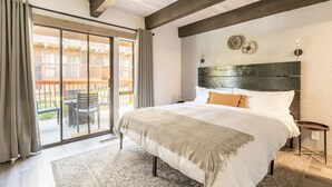 A bedroom with a large bed, a wooden headboard, a sliding glass door to a balcony, and a small bedside table. - Feet Away From Slopes Cozy Snow Summit Cabin (Big Bear Lake)