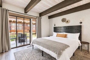 Un dormitorio con una cama grande, cabecera de madera, puerta corrediza de vidrio a un balcón y una mesita de noche pequeña.