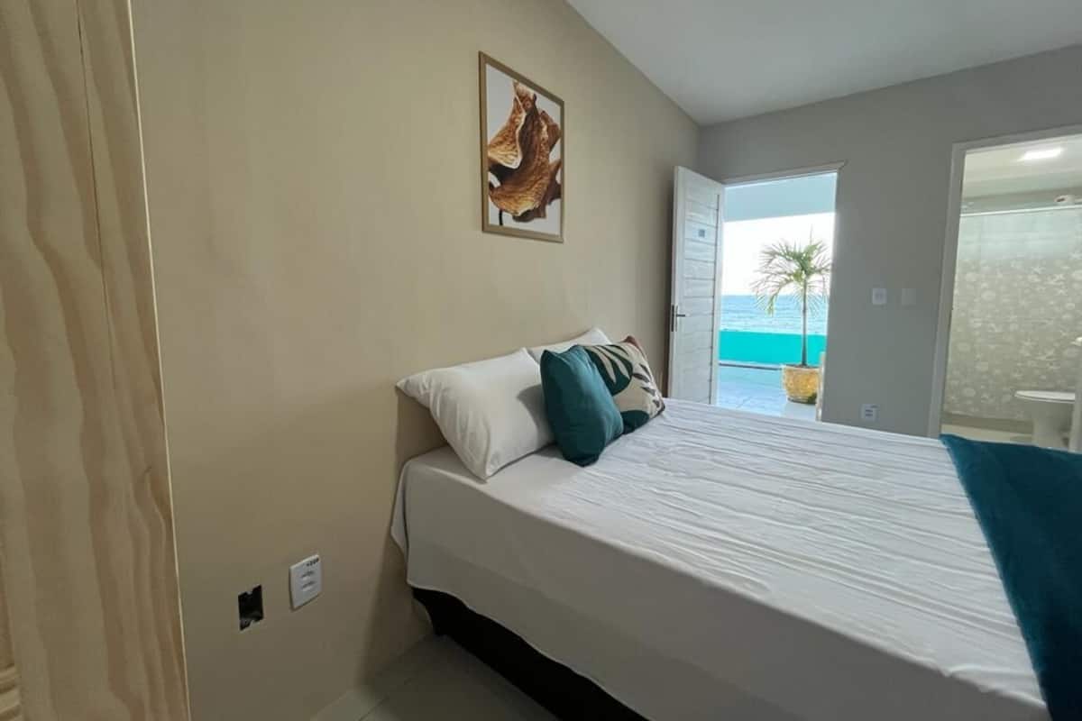 Ein Schlafzimmer mit Bett, einem Bild an der Wand und Blick auf das Meer durch eine geöffnete Tür.