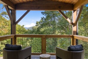Terraza de madera con mobiliario de mimbre y vista a árboles y montañas.